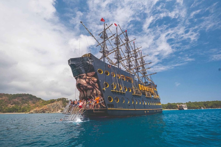 A large ship with a dragon sculpture on its side, sailing in a body of water with a clear sky and a hilly coastline in the background. 1
