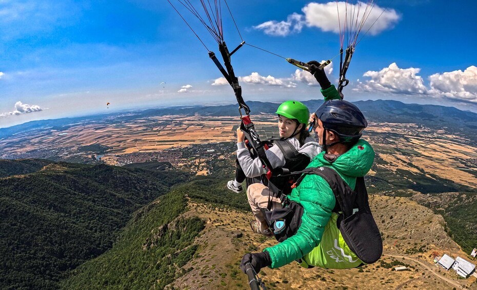 Two people paragliding over a mountainous landscape with a clear sky. 3