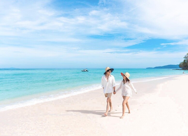 Two people walking on a white sandy beach with clear turquoise water and a boat in the distance. 3