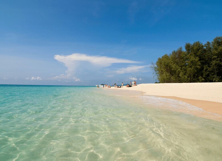 A beach with clear turquoise water, white sand, and a line of trees in the background. 2