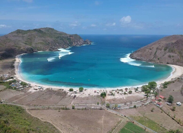 A coastal landscape with a beach, clear blue waters, and surrounding hills. 2