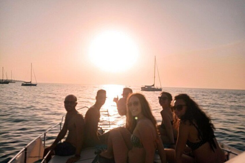 A group of people on a boat at sunset with sailboats in the background. 4