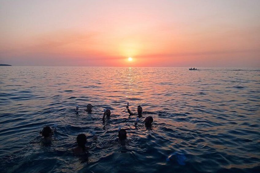 A sunset over a calm sea with people swimming. 5