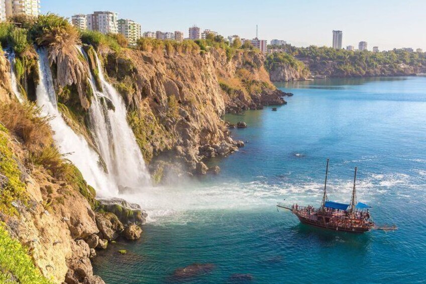 Escena costera con una cascada, un bote y el perfil de una ciudad al fondo. 1