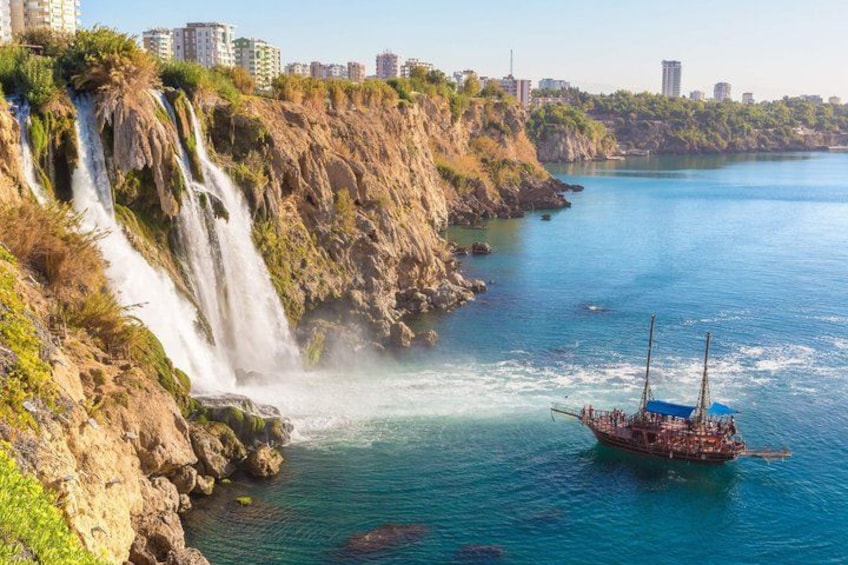 A coastal scene with a waterfall, a boat, and a city skyline in the background. 1