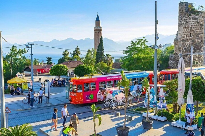 Eine belebte Straße mit bunten Bussen, Fußgängern und einem historischen Turm im Hintergrund. 5