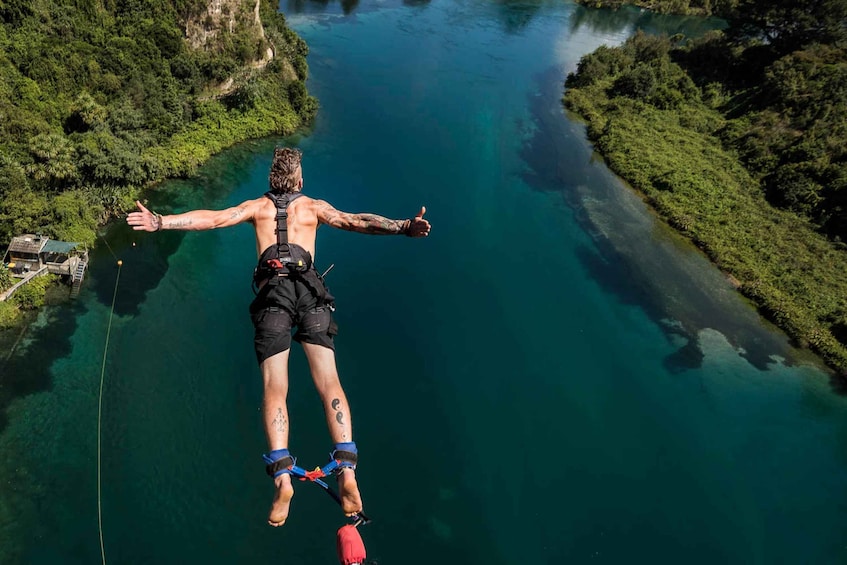 A person bungee jumping with arms outstretched over a river surrounded by greenery. 3