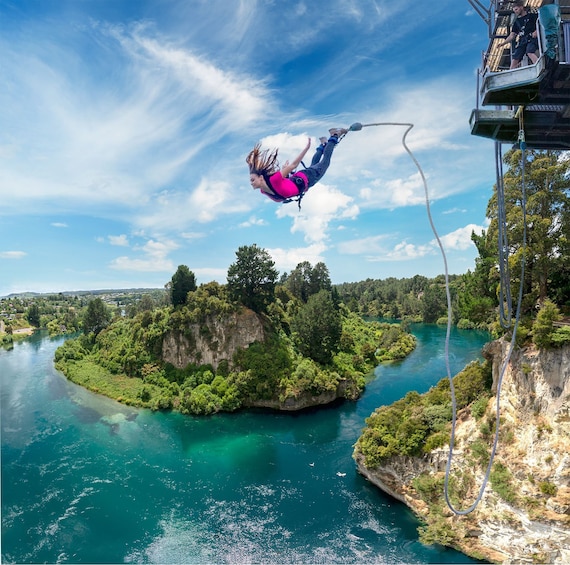 A person bungee jumping off a high platform with a river and cliffs in the background. 1