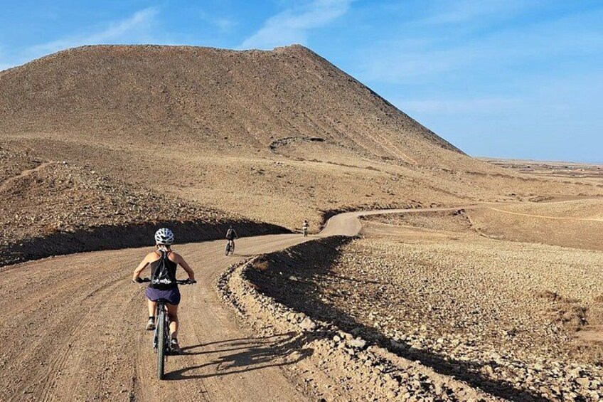 Un ciclista en un camino de tierra con terreno rocoso y una colina al fondo. 2