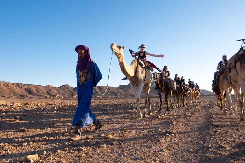 A camel caravan in a desert landscape with rocky terrain and distant mountains. 2