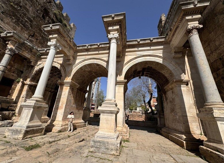 An ancient stone archway with columns, a person standing in the foreground, and a clear blue sky in the background. 1