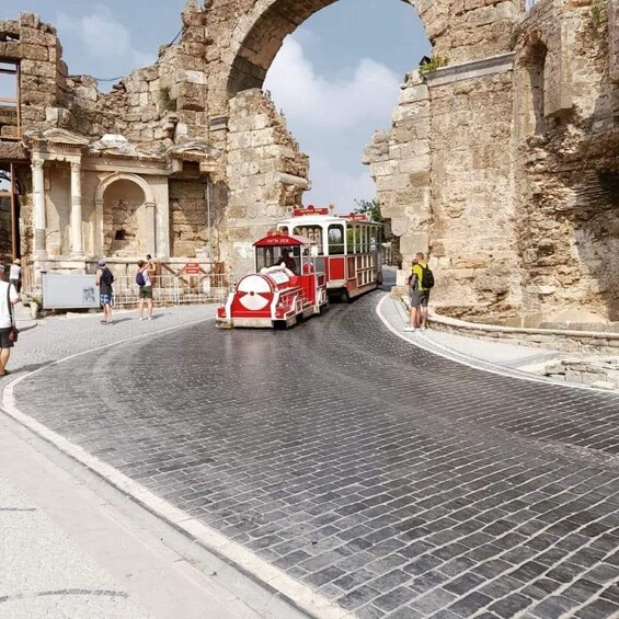 A red and white tram moving through an ancient stone archway. 5