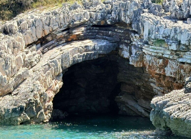 A natural rock formation with a cave entrance and clear blue water at the base. 3