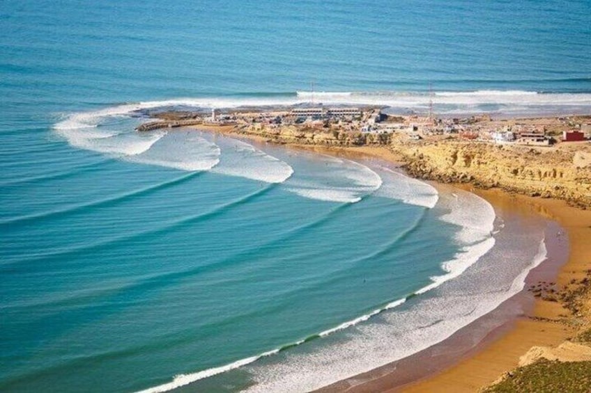 A coastal landscape with a sandy beach, waves, and a distant shoreline with buildings. 1