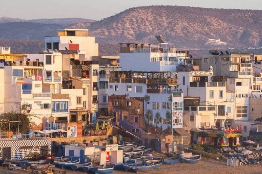 A coastal town with multi-story buildings, a beach with boats, and a mountainous backdrop. 3