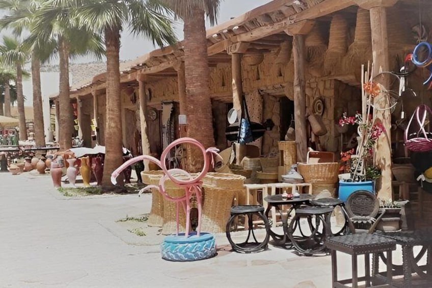 A rustic outdoor market with wooden stalls, palm trees, and various items for sale. 5