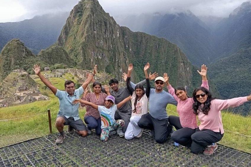 A group of people posing with their arms raised in front of a mountainous landscape. 2