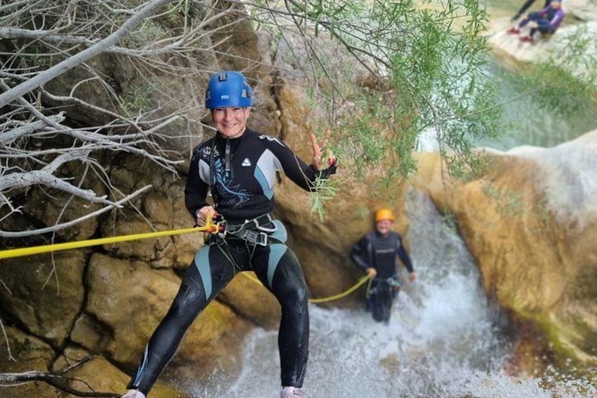 A person rappelling down a rocky cliff with a harness and helmet, another person in the background, and a waterfall. 4