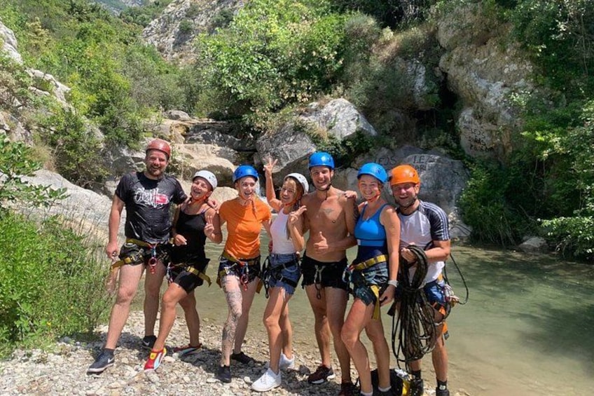 A group of people wearing helmets and harnesses, standing on a rocky riverbank. 5