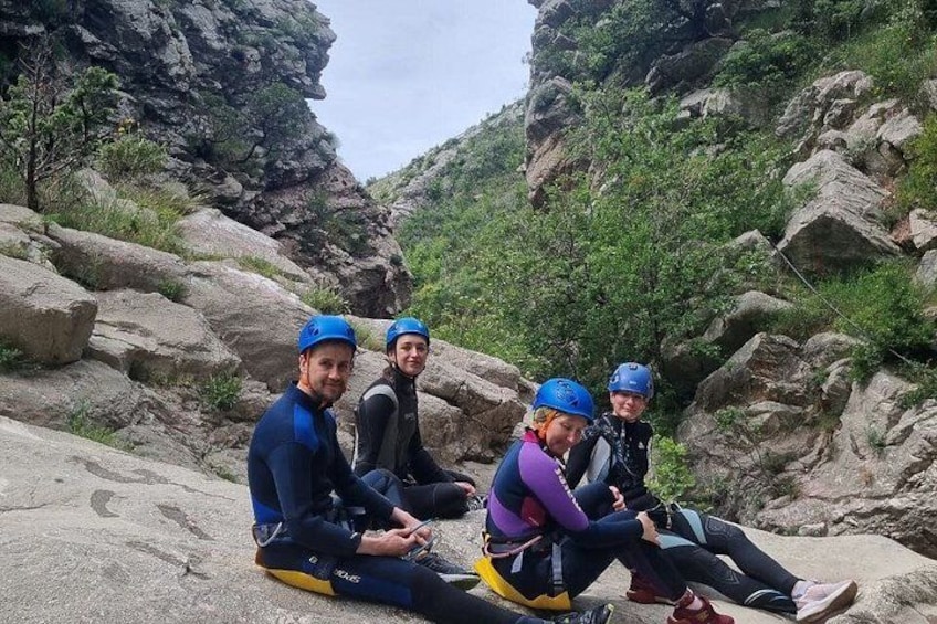Four people sitting on a rocky surface in a canyon with greenery in the background. 3