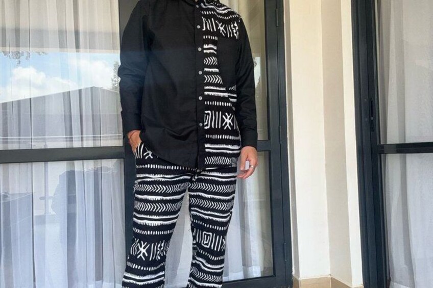 En person står indendørs iført bukser med et mønster og en sort skjorte. 2