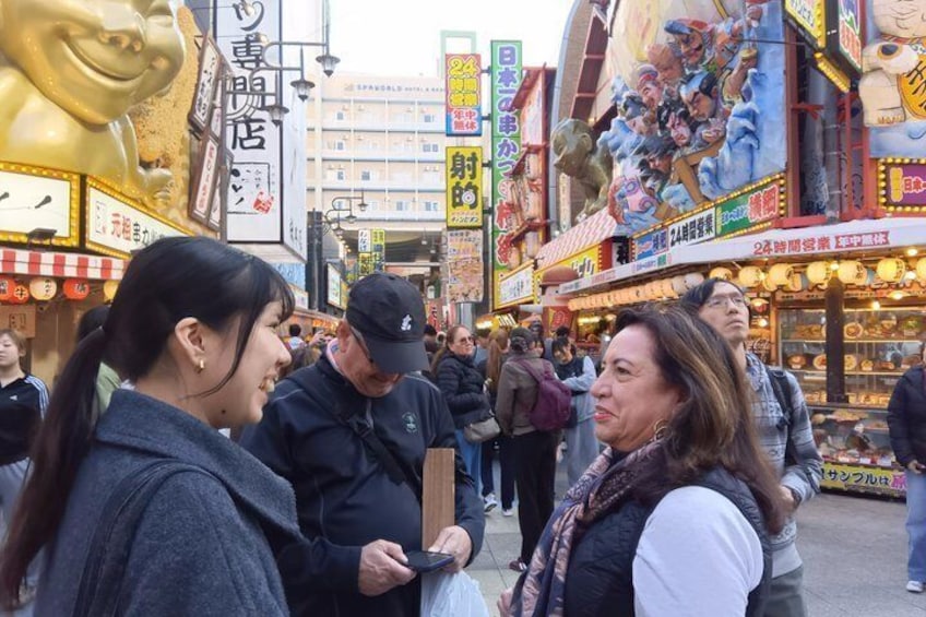Una calle animada con gente, tiendas y una gran estatua dorada. 2