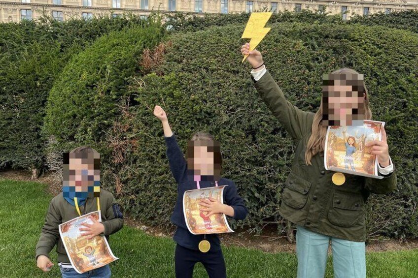 Three individuals holding books and a lightning bolt, standing in front of a hedge. 1