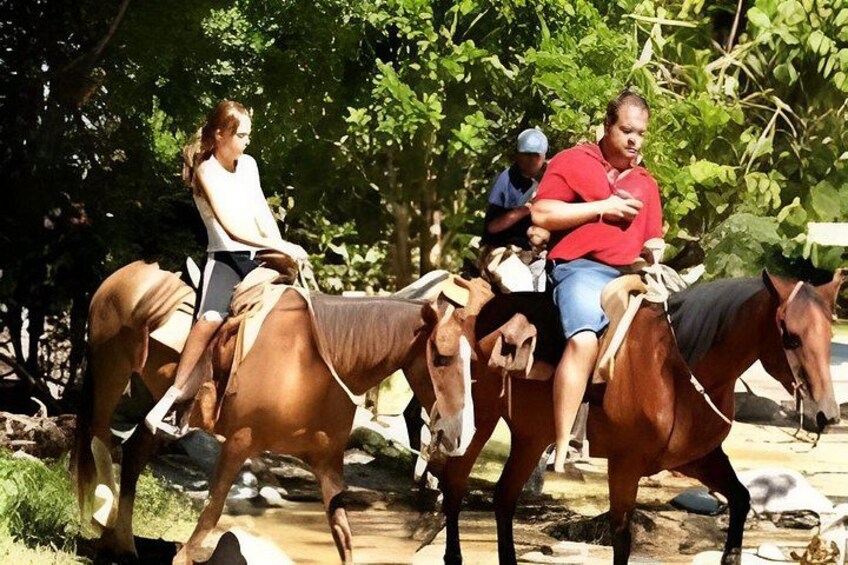 Three people riding horses on a dirt path surrounded by trees. 1