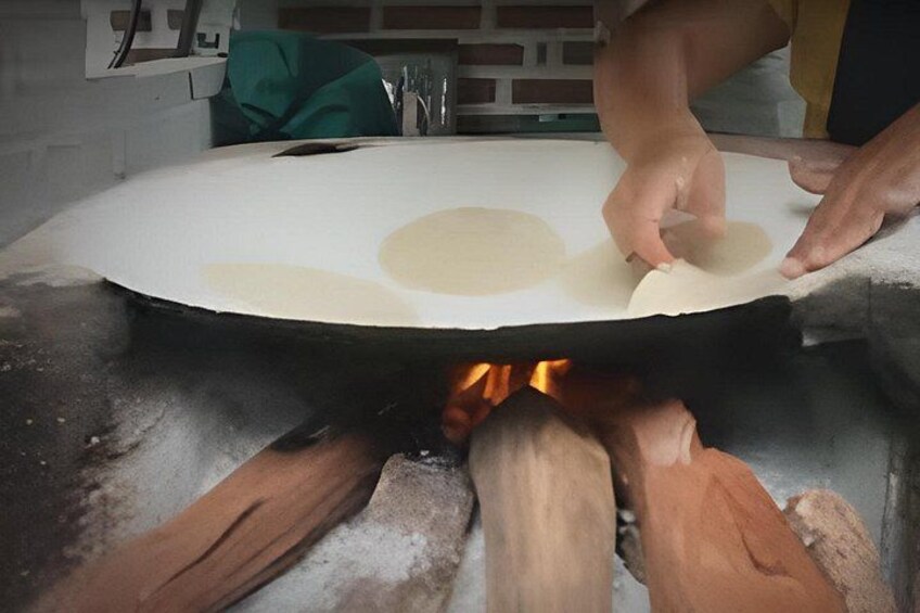 A person placing dough on a flat surface above a wood-fired oven. 4