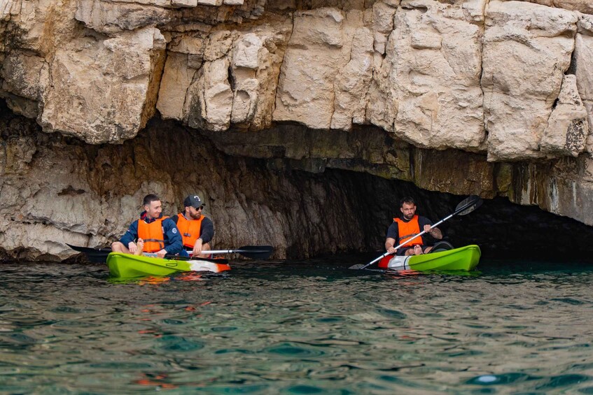 Three people kayaking in a green kayak near a rocky cave entrance. 3