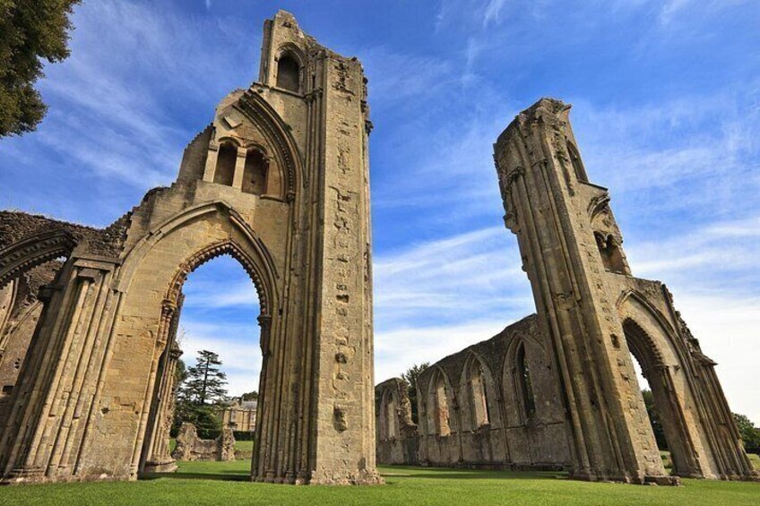 A historic stone structure with arches and columns, surrounded by grass and trees. 2