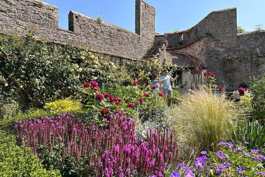 A garden with stone walls, flowering plants, and a person walking. 3