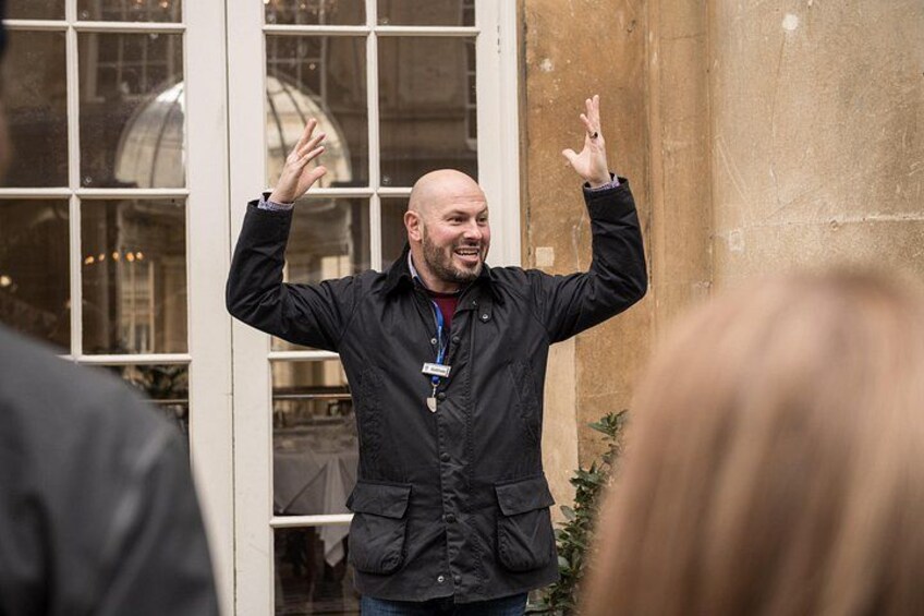 A person in a black jacket with raised hands, standing in front of a building with large windows and a dome structure. 2