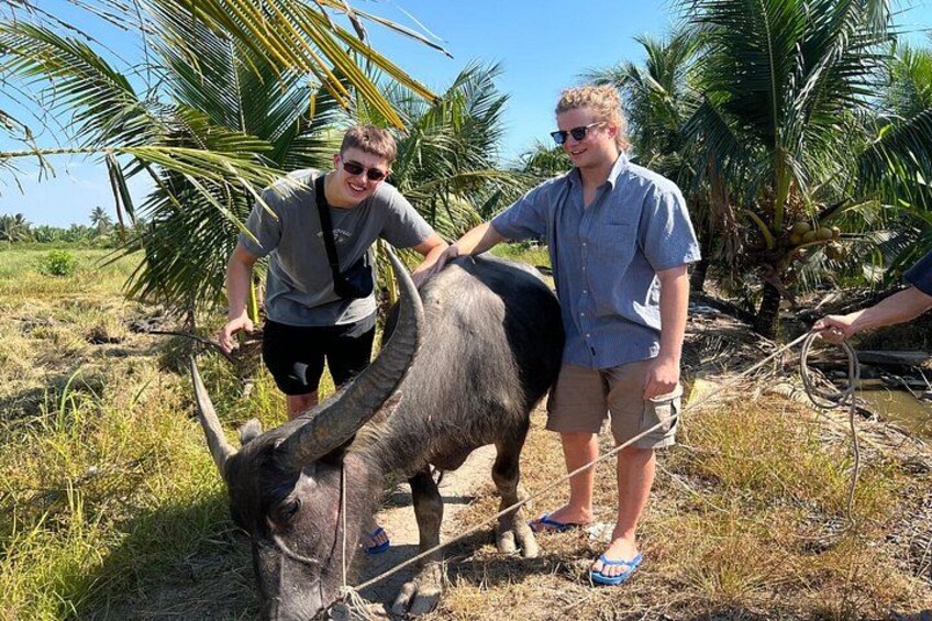 Twee personen in een grasrijke omgeving met palmbomen, interactie met een groot, donker neushoorn. 2