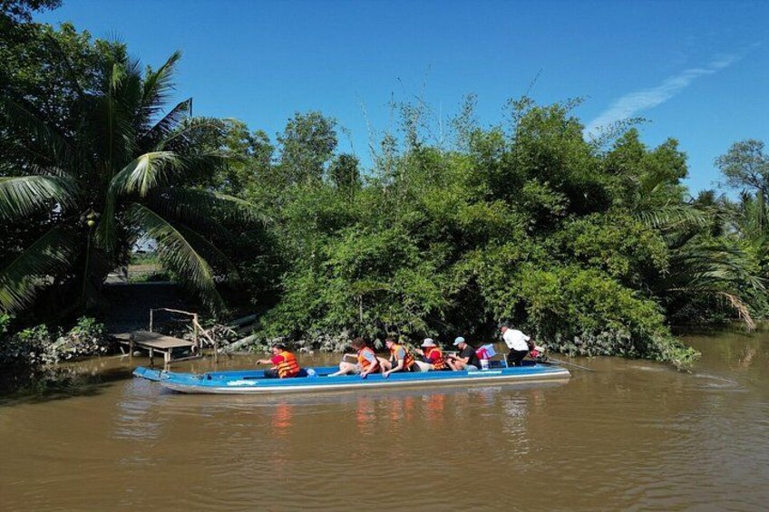 Een groep mensen op een blauwe boot in een rivier, omgeven door weelderige begroeiing. 1