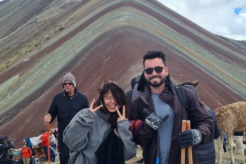 A group of people standing on a mountain with a colorful geological formation in the background. 4