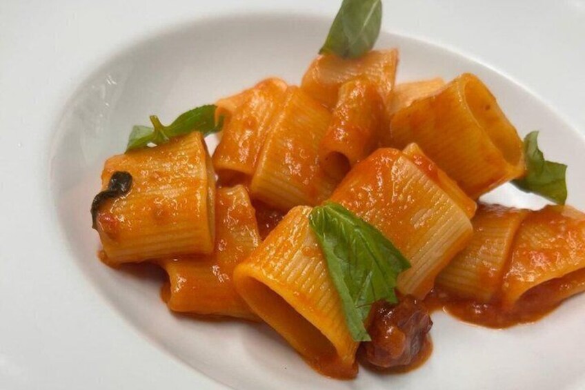 A plate of cooked rigatoni pasta with a tomato-based sauce and garnished with basil leaves. 5