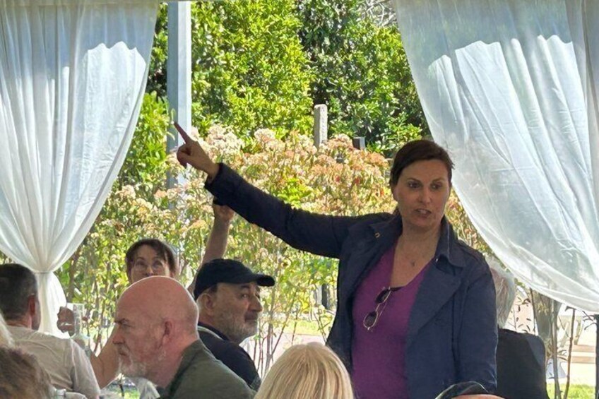 A person speaking to an audience under a white canopy in an outdoor setting. 2