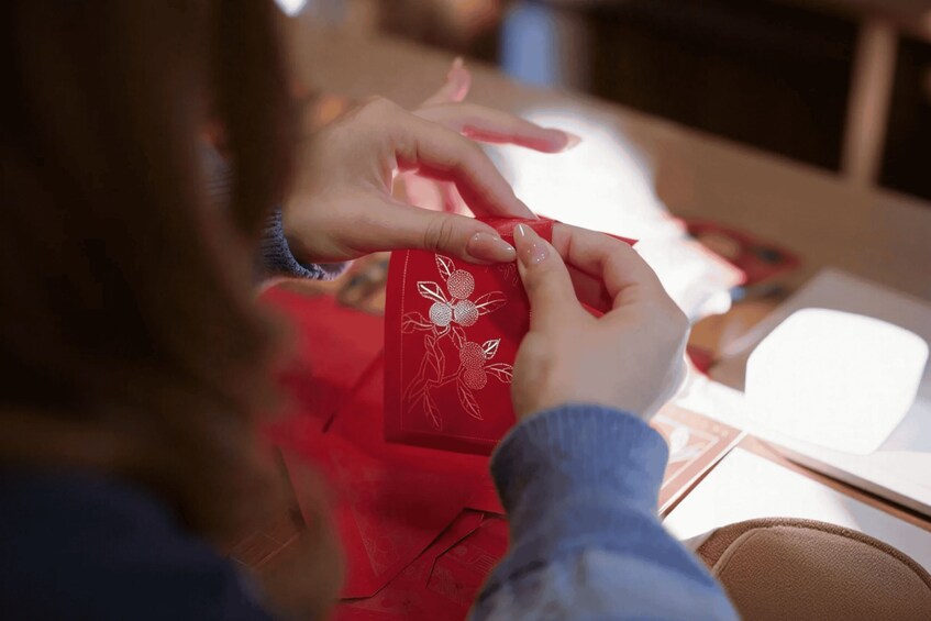 A person sewing a red fabric with a floral pattern. 5