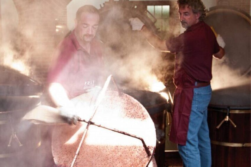 Dos personas cocinando con una parrilla grande, vapor ascendiendo y un barril al fondo. 4