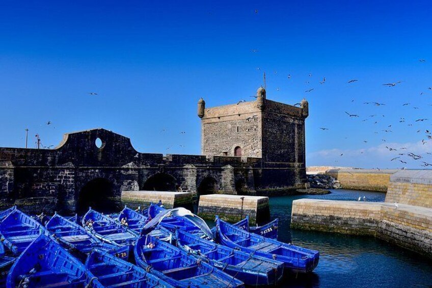 A historic stone tower, a harbor with blue boats, and a clear blue sky. 1