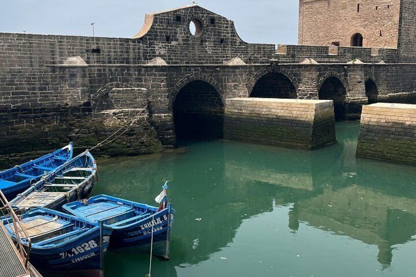 A stone bridge with arched passageways over a body of water, boats docked at the pier, and a brick tower in the background. 2