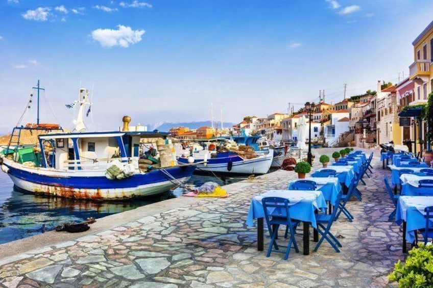 Un puerto con barcos amarrados, paseos de adoquines y mesas azules preparadas para comer al aire libre. 4