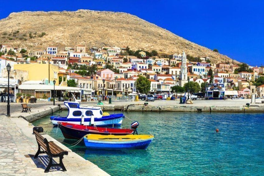 Un pueblo costero con coloridas embarcaciones amarradas en el puerto, un banco de piedra y edificios en una ladera. 1