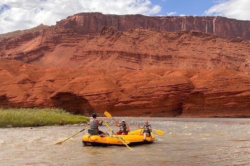 Two people kayaking on a river with red rock formations in the background. 1