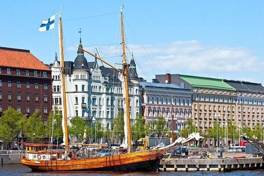 A tall ship docked at a harbor with historic buildings in the background. 1