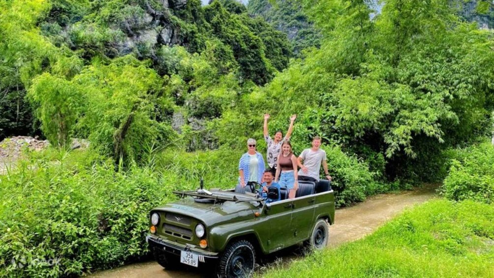 A group of people in a green vehicle on a dirt path surrounded by lush greenery. 5