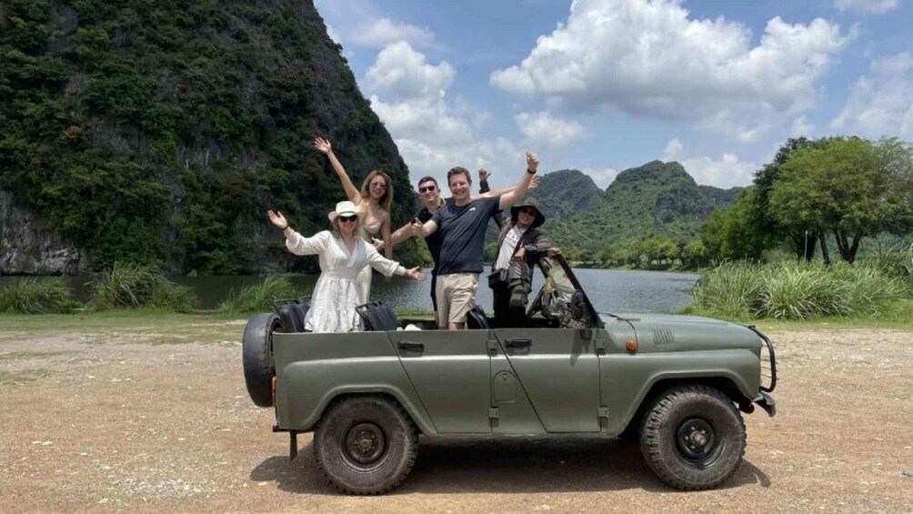A group of people on a green off-road vehicle in a natural setting with a lake and mountains in the background. 3