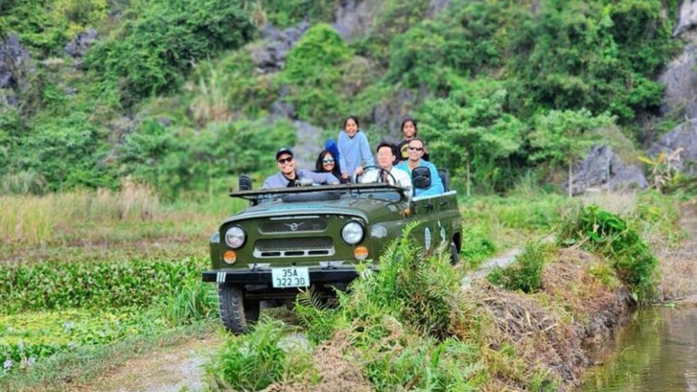 A group of people in a green off-road vehicle on a narrow path surrounded by greenery. 2