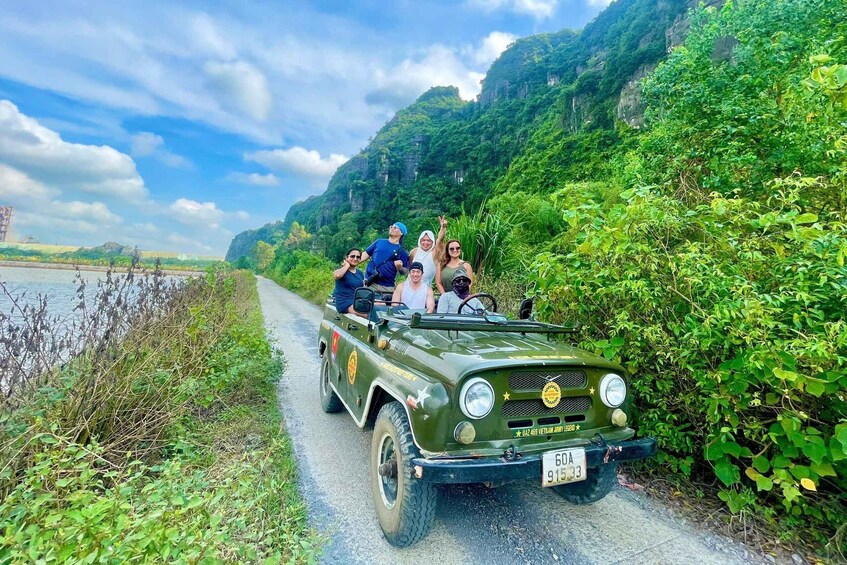 A green jeep with passengers on a road flanked by lush greenery and cliffs. 4